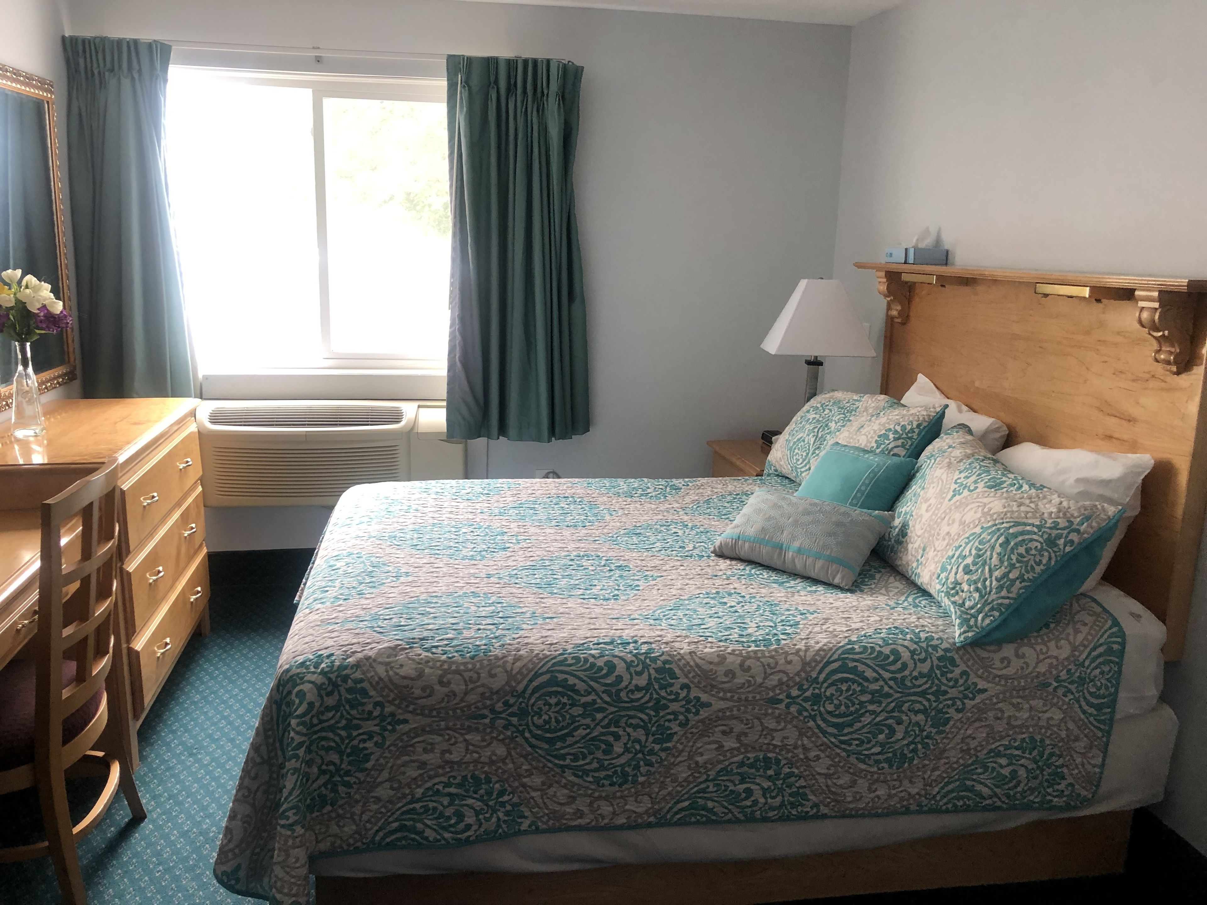 A bedroom with a bed, dresser, and window with curtains.