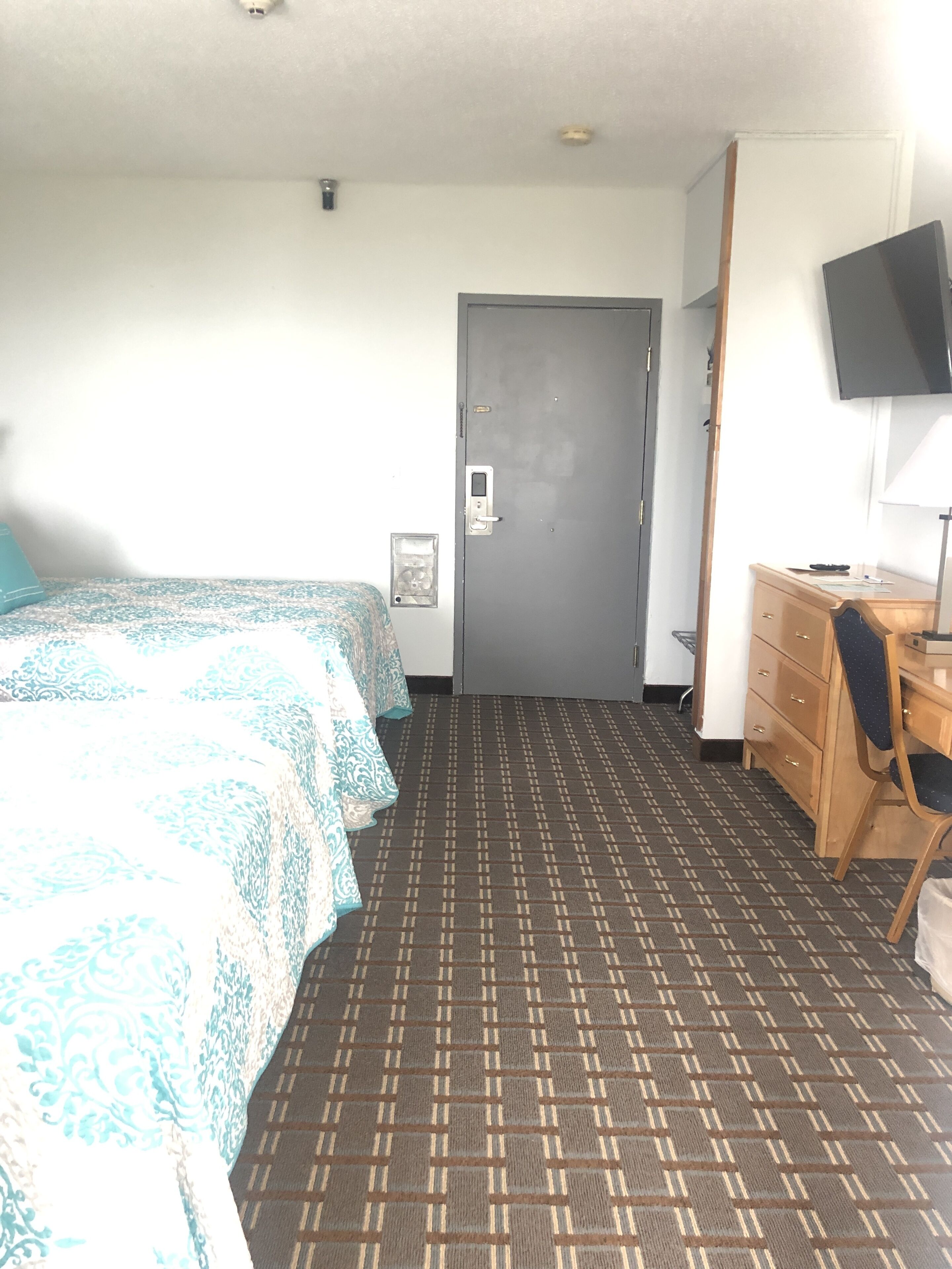 Ett hotellrum med en säng, ett skrivbord, en stol, en tv och en dörr.