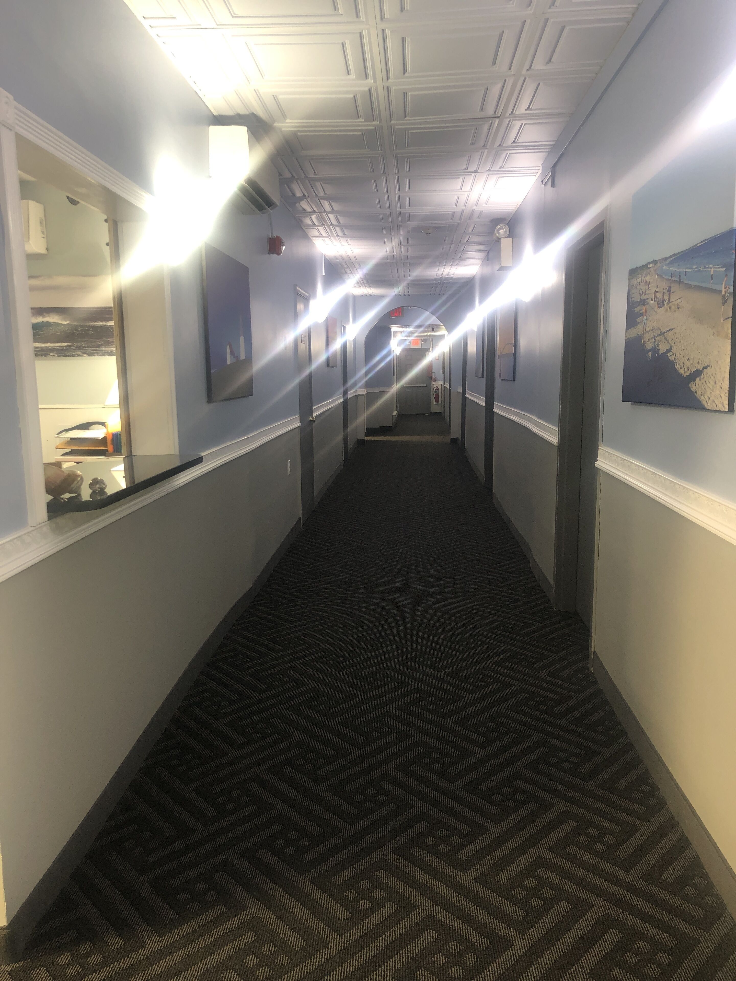 Un pasillo de hotel con alfombra estampada, paredes blancas e iluminación empotrada en el techo.