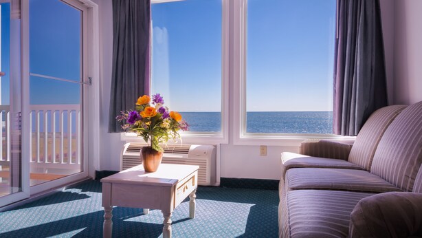 A room with a view of the sea, a sofa, a small table with a vase of flowers, and a window with curtains. - Atlantic House (Narragansett)