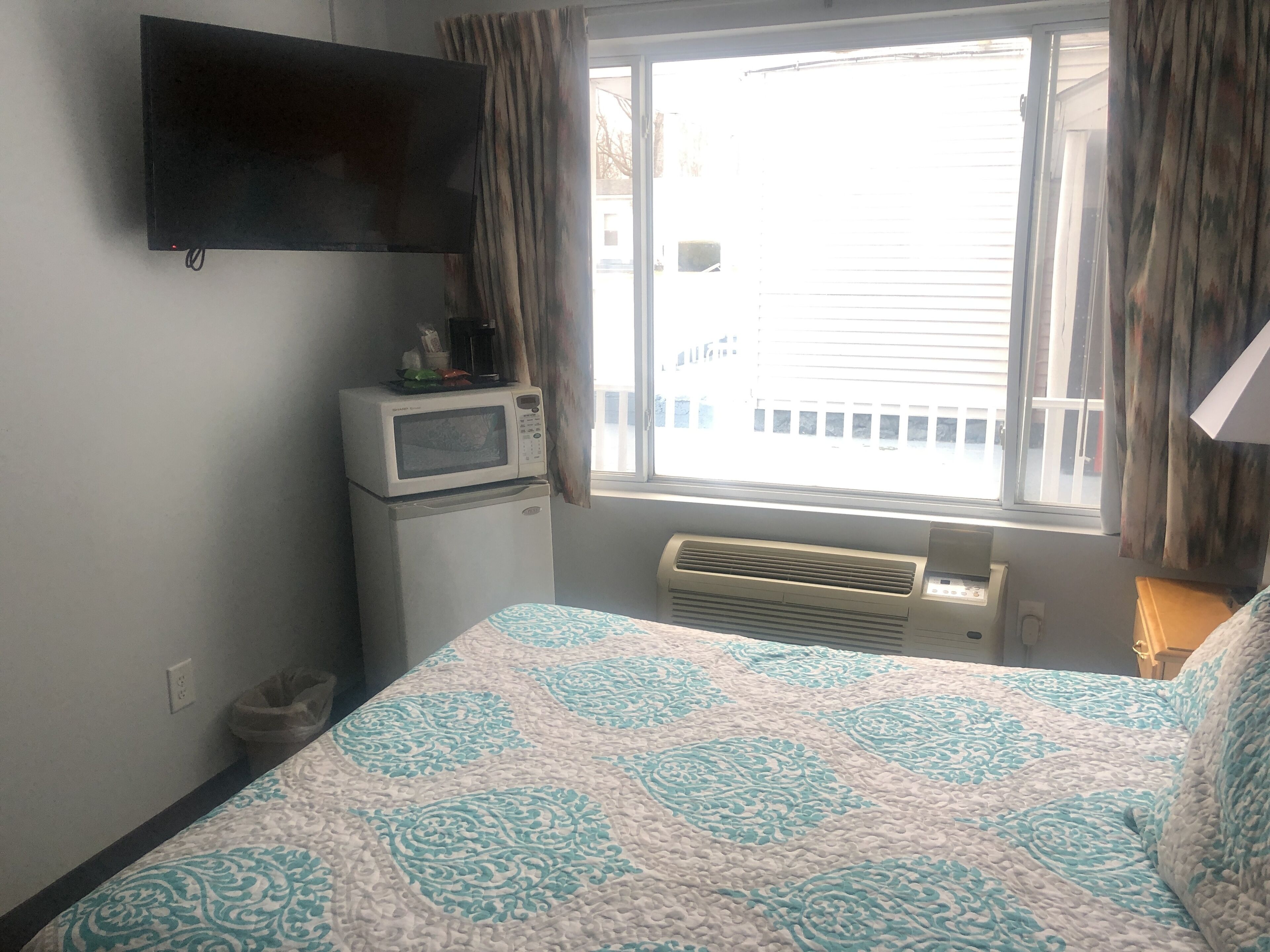 Un dormitorio con cama, televisor de pantalla plana en la pared, microondas y aire acondicionado.