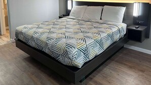 A modern bed with a geometric patterned bedspread, a dark headboard, and bedside lamps. - Studio 6 Vicksburg, MS - Downtown (Vicksburg)