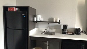 A compact kitchenette with a black refrigerator, a coffee maker, a toaster, and a microwave. - Studio 6 Vicksburg, MS - Downtown (Vicksburg)