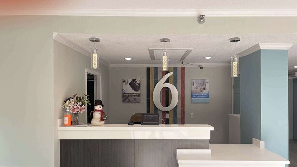A reception desk with a large number '6' sign, a vase with flowers, and a framed picture on the wall. - Studio 6 Vicksburg, MS - Downtown (Vicksburg)