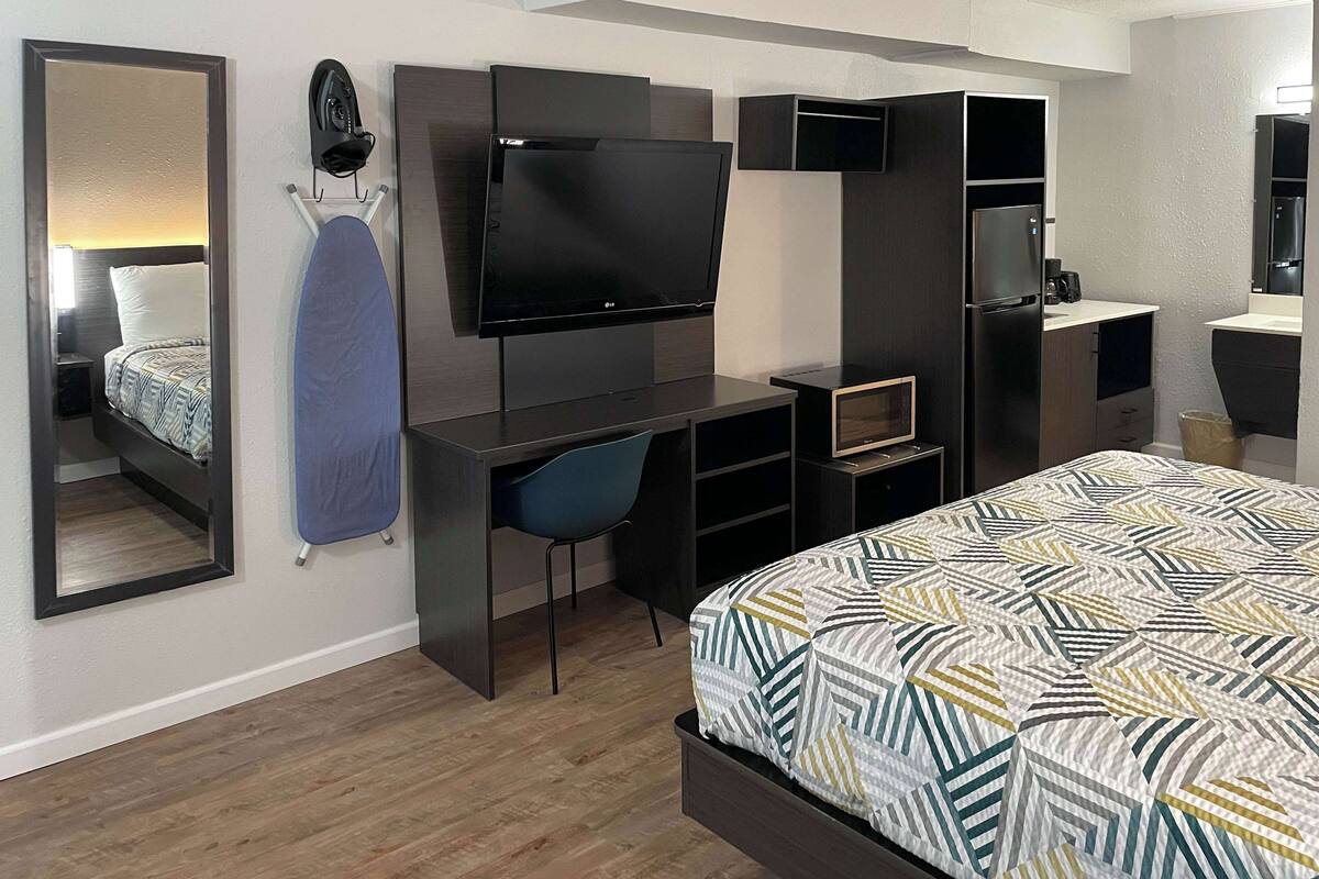 A modern hotel room with a large bed, a desk with a chair, a flat-screen TV, a mirror, and built-in storage cabinets.