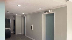 A hallway with a grey tiled floor, a door with a handle, and a sign above the door. - Studio 6 Vicksburg, MS - Downtown (Vicksburg)
