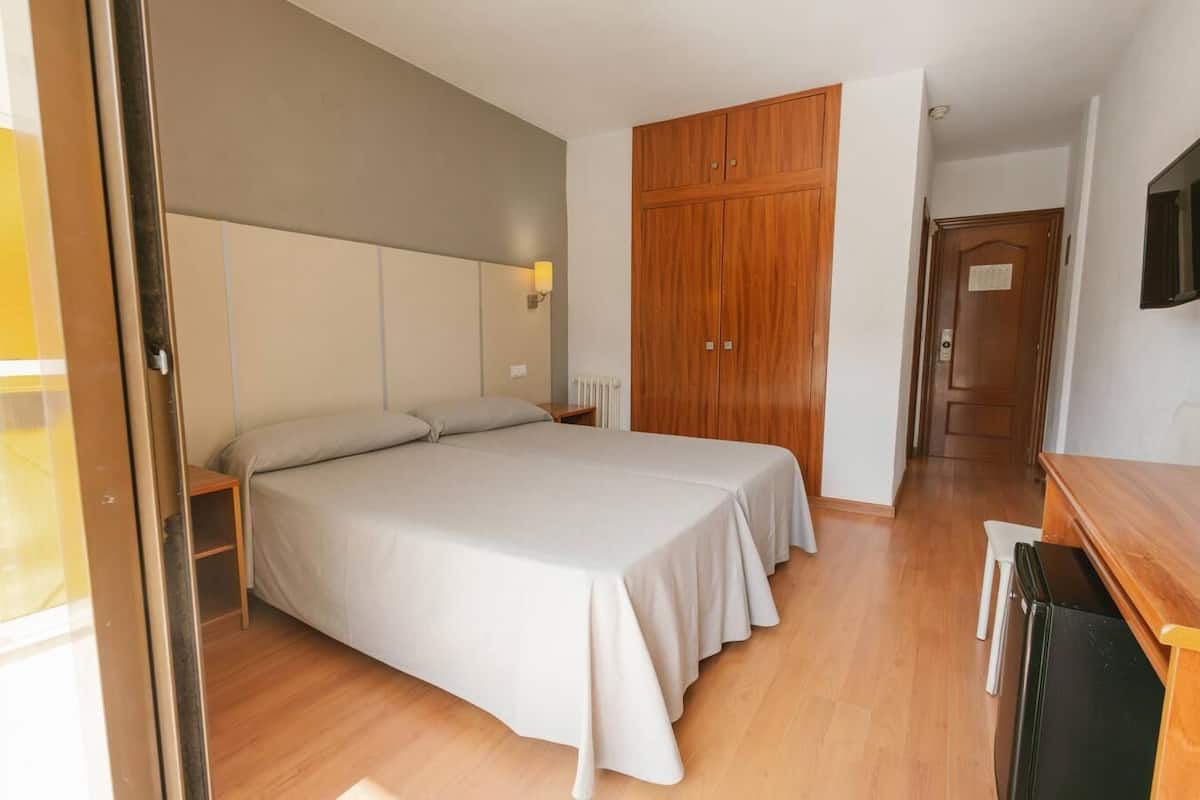 A bedroom with a large bed, wooden wardrobe, and a small table.