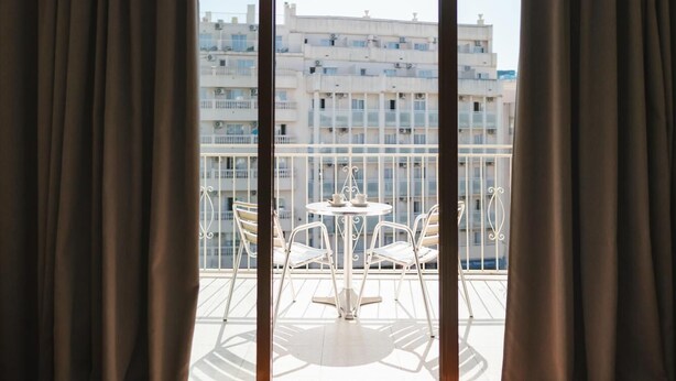 Un balcon avec une table et des chaises, donnant sur un paysage urbain composé de nombreux immeubles.