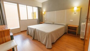 Une chambre d’hôtel avec un lit double, une petite table, une chaise, une table de chevet, un radiateur et une fenêtre avec des rideaux.