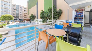 Un espace piscine aménagé sur le toit, avec des chaises colorées et une petite table, entouré d’immeubles et de verdure.