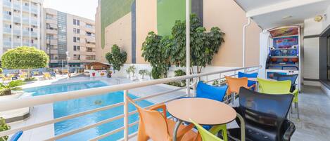 A rooftop pool area with colorful chairs and a small table, surrounded by buildings and greenery.