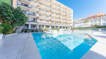 Un hotel de varios pisos con piscina, balcones y un cielo azul despejado.
