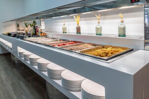 A buffet with various food items and condiments, neatly arranged on a counter with stacked plates below.
