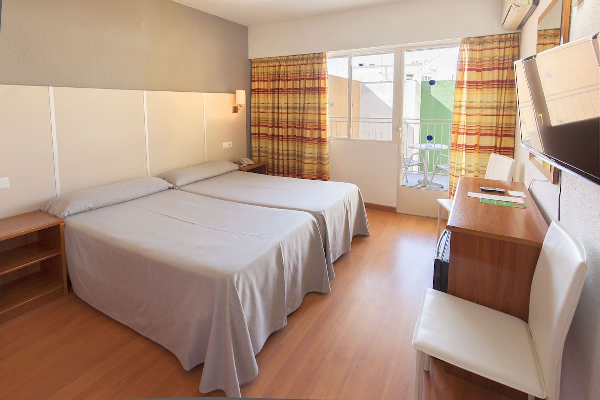 A hotel room with two beds, a desk, a chair, a TV, and a window with curtains.