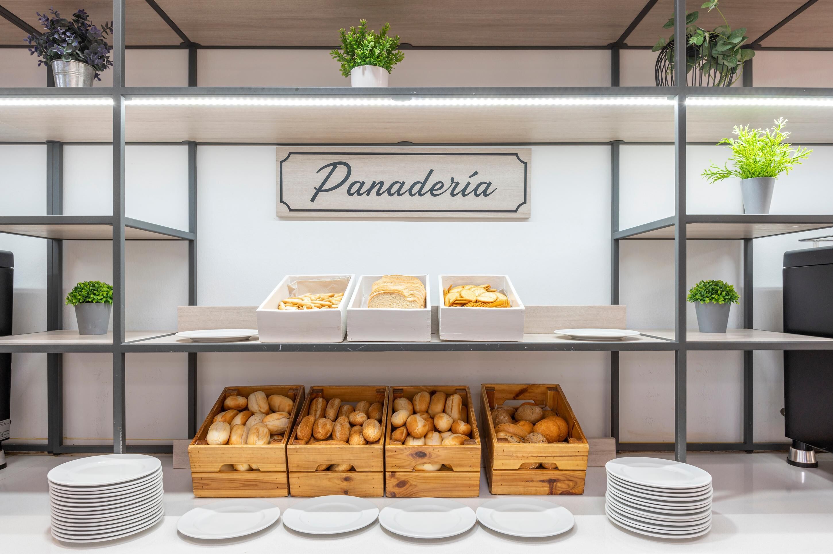 A bakery counter with labeled sections for bread and pastries, surrounded by wooden crates of bread and white plates.
