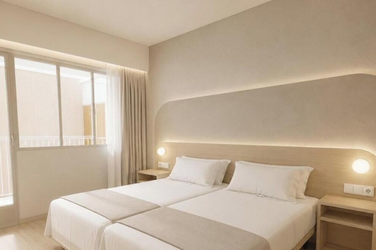 Habitación de hotel con una cama grande, dos mesitas de noche, una ventana con cortinas y un aplique de pared.