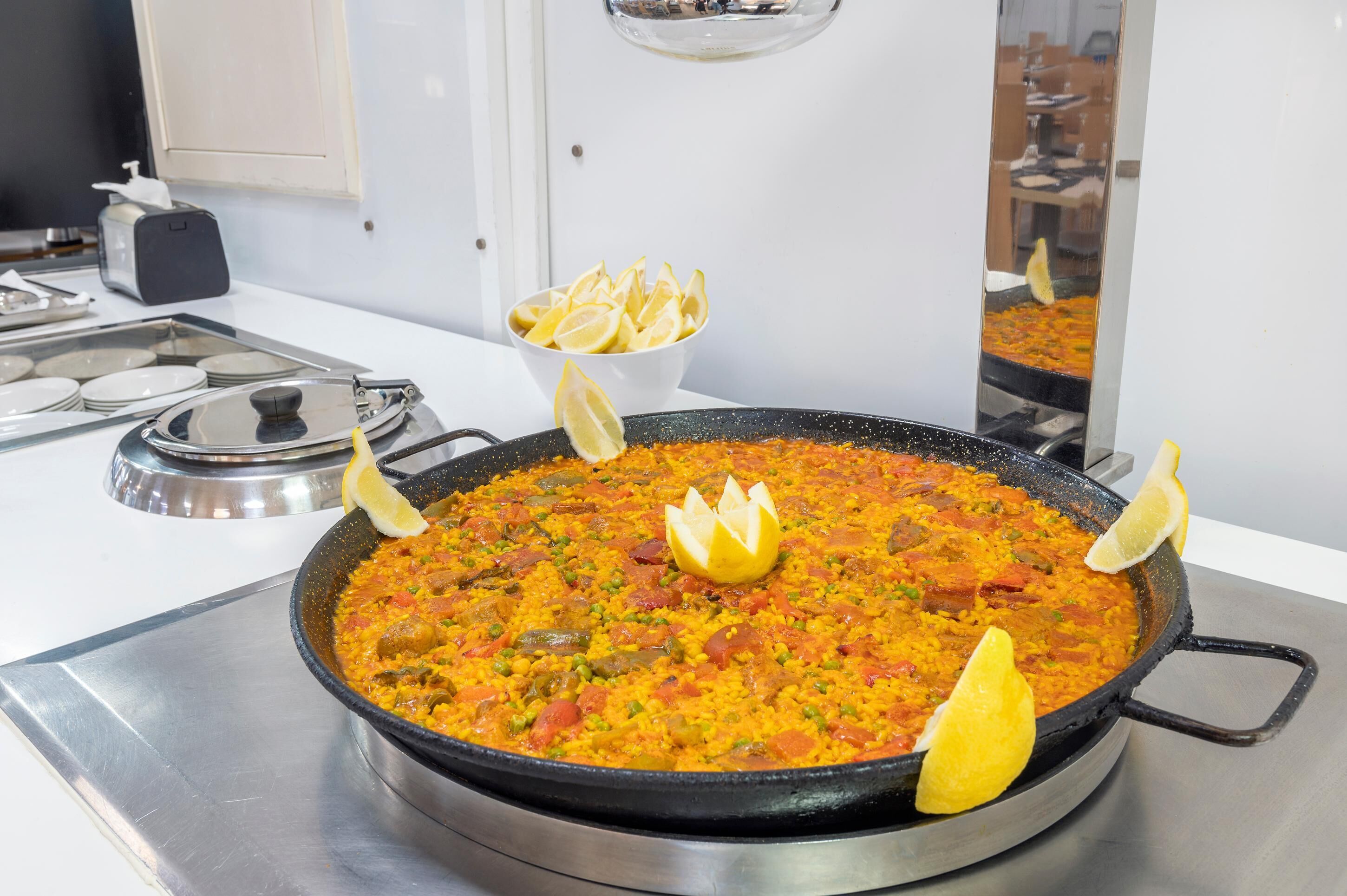 A large pan of paella with lemon wedges on a stove.