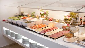 Un buffet proposant une variété de plats, notamment des viandes, des fromages et des légumes, présentés sur un comptoir blanc surmonté d’une vitre.