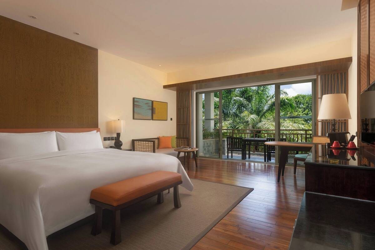 Une chambre d’hôtel avec un grand lit, un bureau, une chaise et un balcon donnant sur un paysage verdoyant.