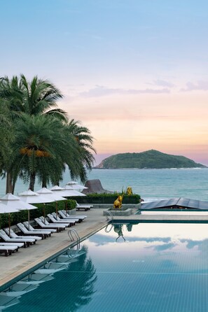 A poolside area with lounge chairs and umbrellas, a statue, and a view of the sea and a distant island. - Le Meridien Shimei Bay Beach Resort & Spa (Wanning)