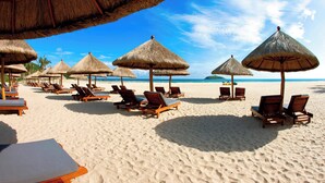 Een strand met rijen ligbedden en rieten parasols.