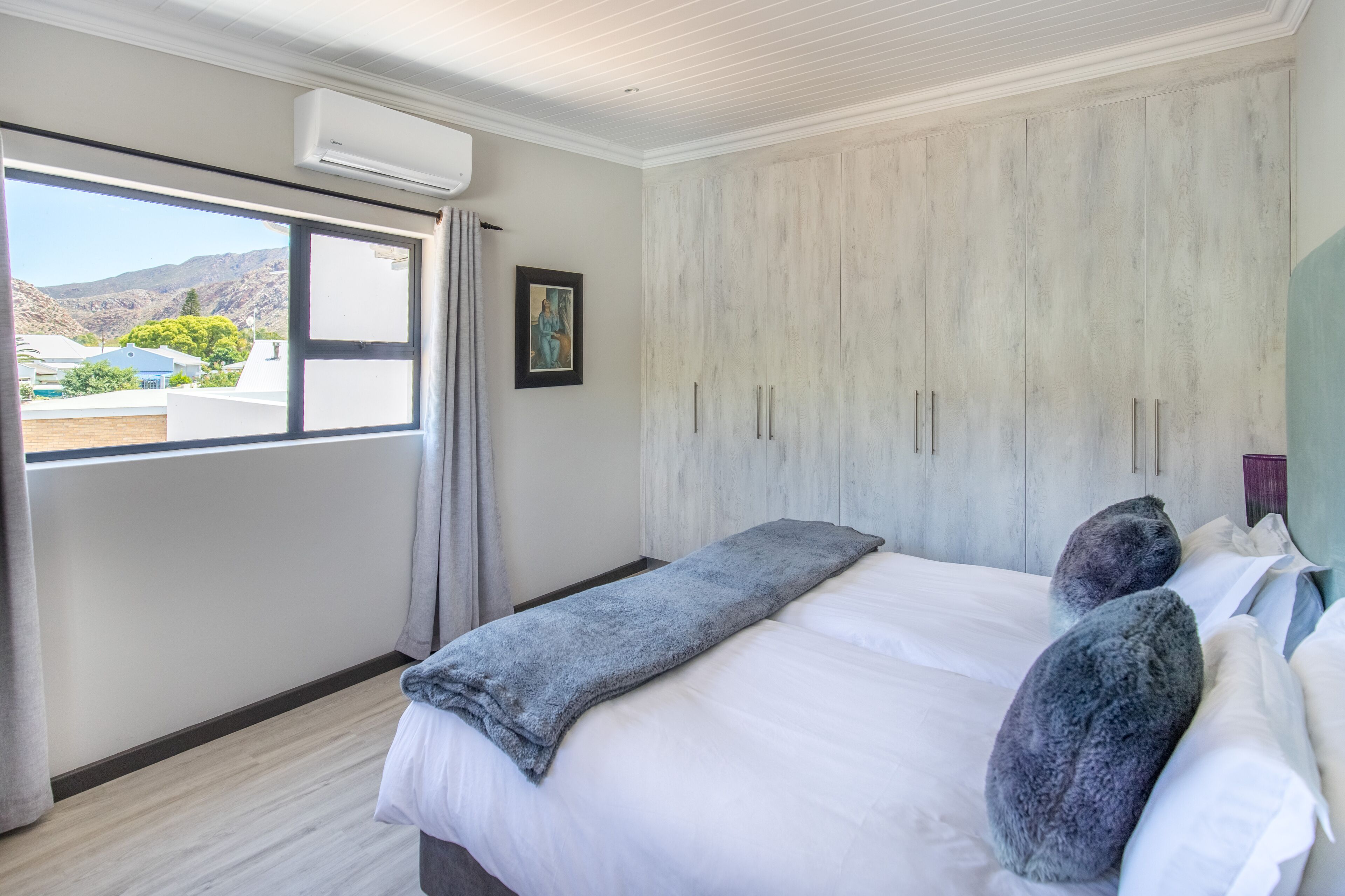 A hotel room with a bed, a large wardrobe, a window with curtains, and a painting on the wall.
