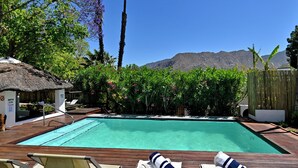 A swimming pool with lounge chairs and a thatched-roof structure. - Mimosa Lodge (Montagu)