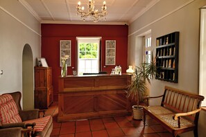 A reception area with a wooden desk, a bench, a potted plant, and artwork on the walls. - Mimosa Lodge (Montagu)
