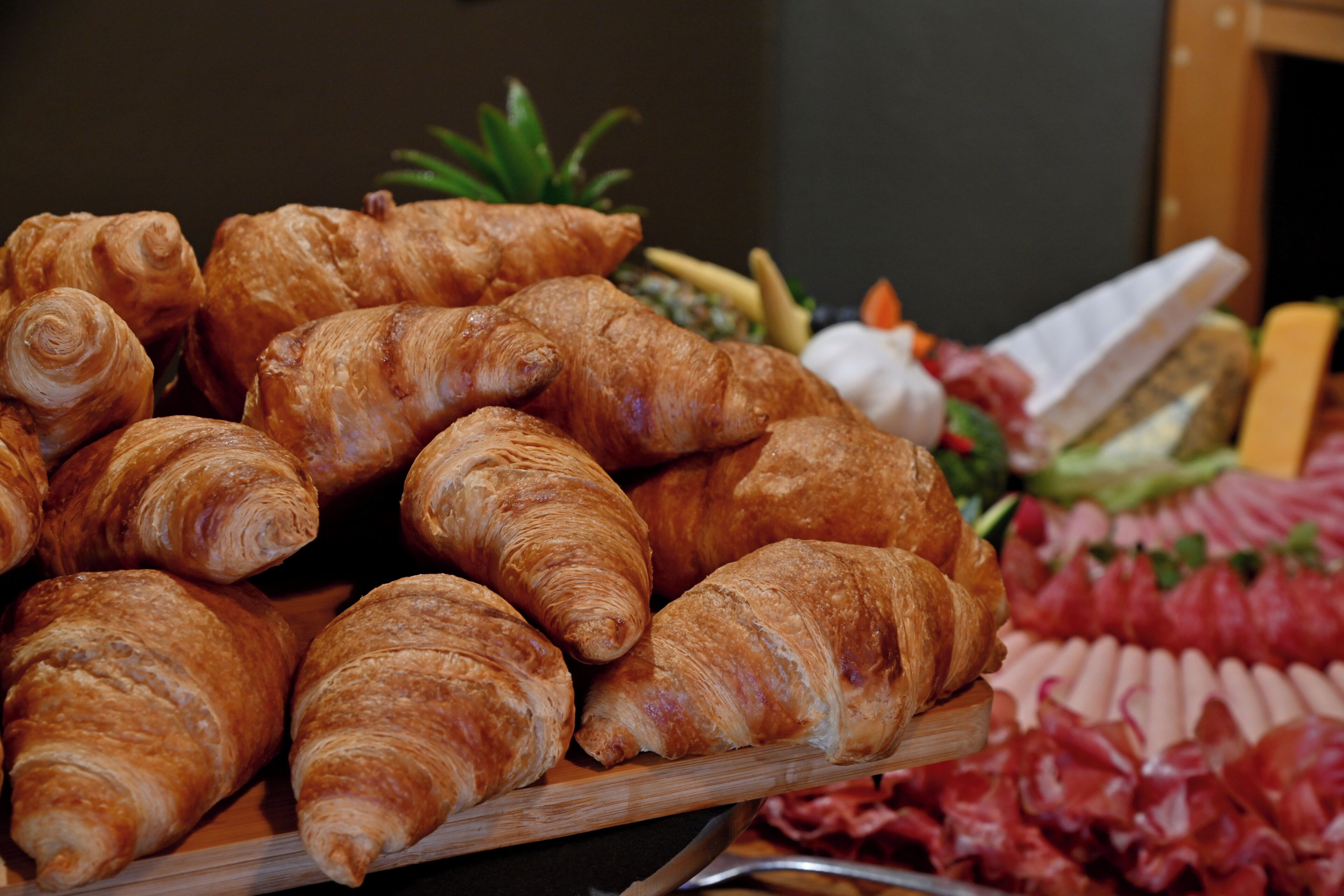 A wooden board with several croissants and a variety of meats.