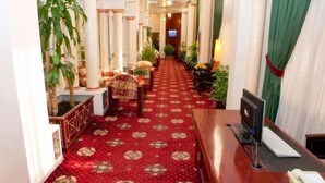 A hotel hallway with a red carpet, wooden furniture, and potted plants. - Safeer Hotel Suites - Aparthotel (Muscat)