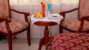 A room with two wooden chairs, a small table with a plate of fruit, a vase, and a glass of orange juice. - Safeer Hotel Suites - Aparthotel (Muscat)