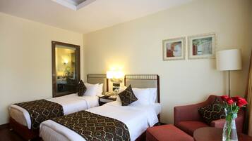 Habitación de hotel con dos camas, una mesita de noche, una lámpara, un florero con flores y un cuadro en la pared.