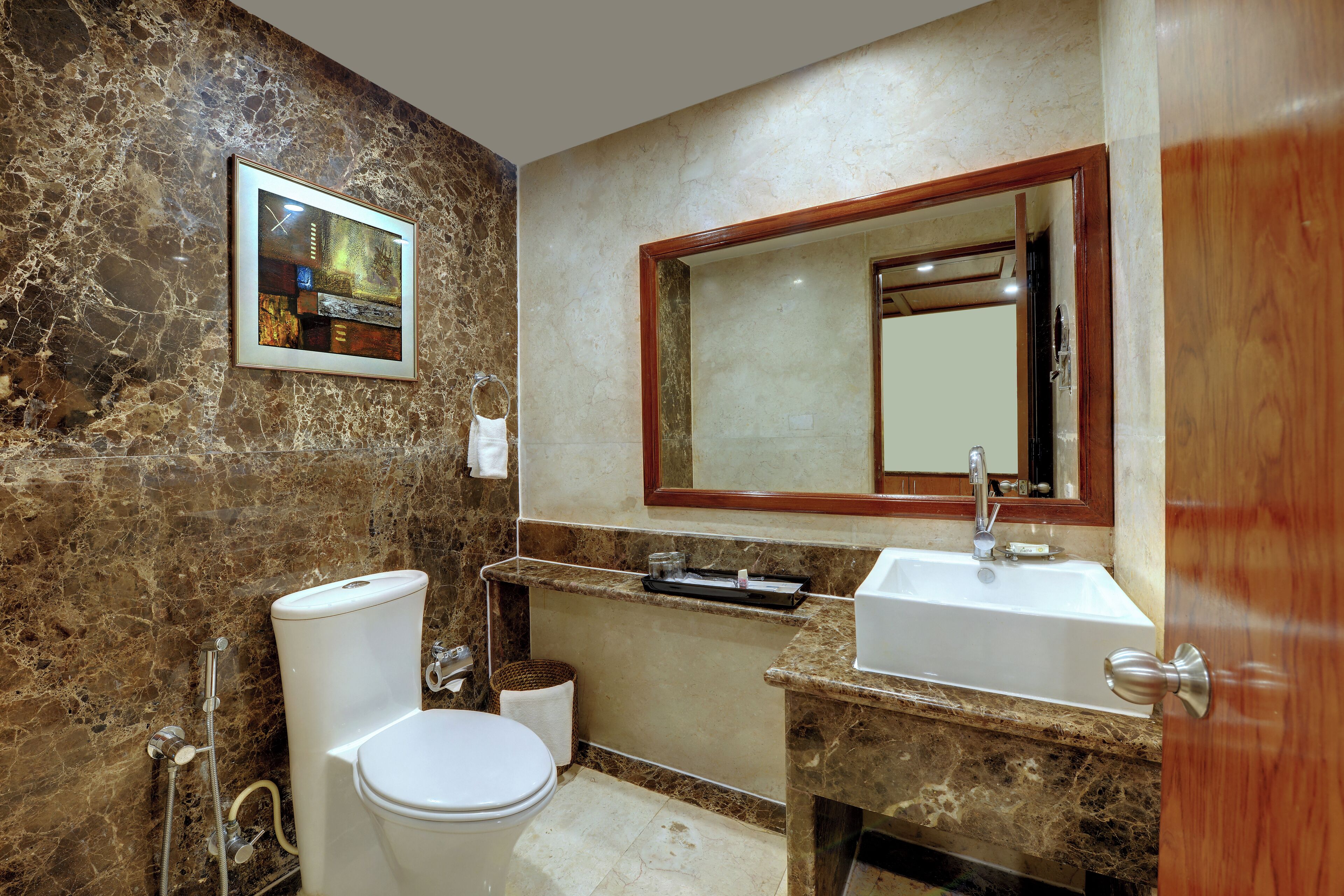 A bathroom with a marble wall, a framed artwork, a sink, and a toilet.