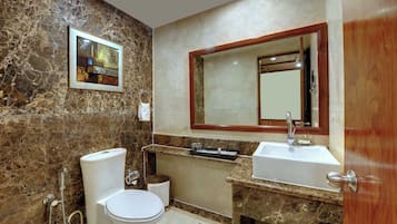 A bathroom with a marble wall, a framed artwork, a sink, and a toilet.