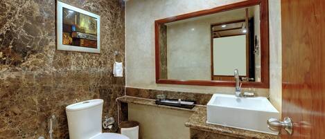 A bathroom with a marble wall, a framed artwork, a sink, and a toilet.