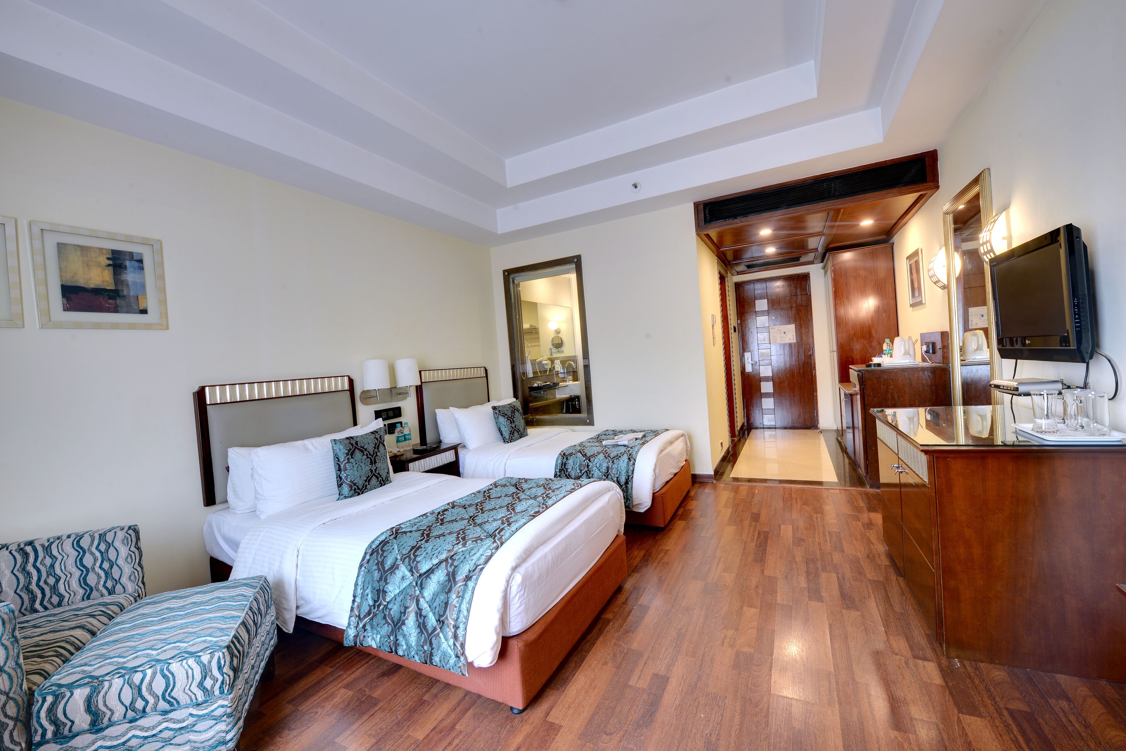 A hotel room with two beds, a desk, a mirror, and a television.