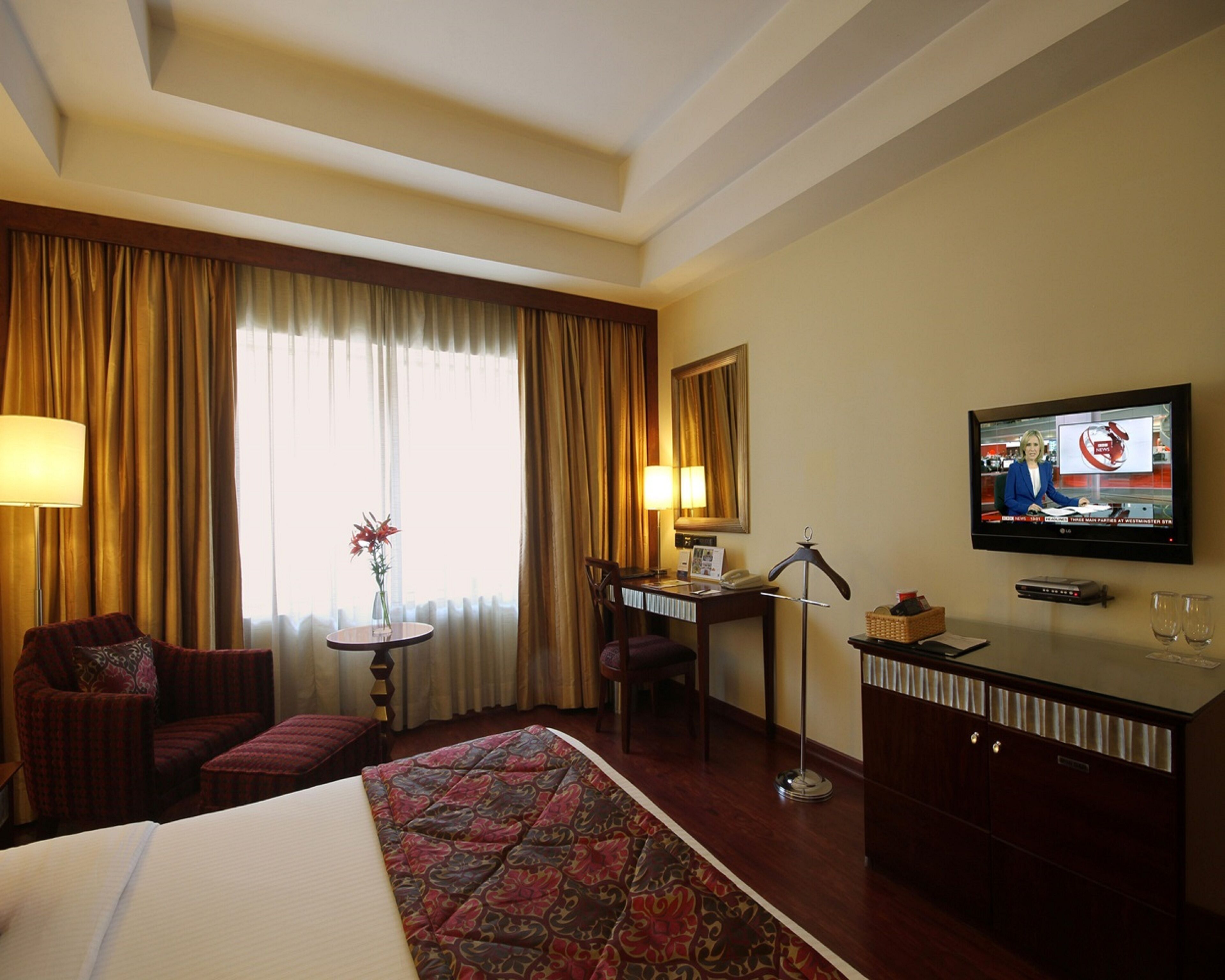 A hotel room with a bed, a desk, a chair, a TV, and a window with curtains.