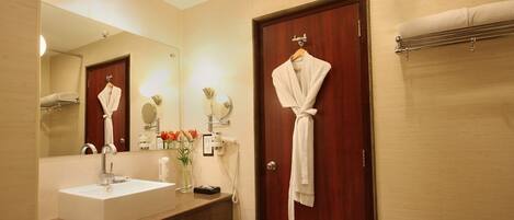Un baño de hotel con un espejo grande, un lavamanos, una bata colgada en la puerta y un perchero para toallas.