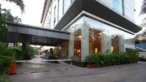 Una entrada de hotel moderna con un vestíbulo cubierto, plantas en macetas y un camino de acceso con portón.