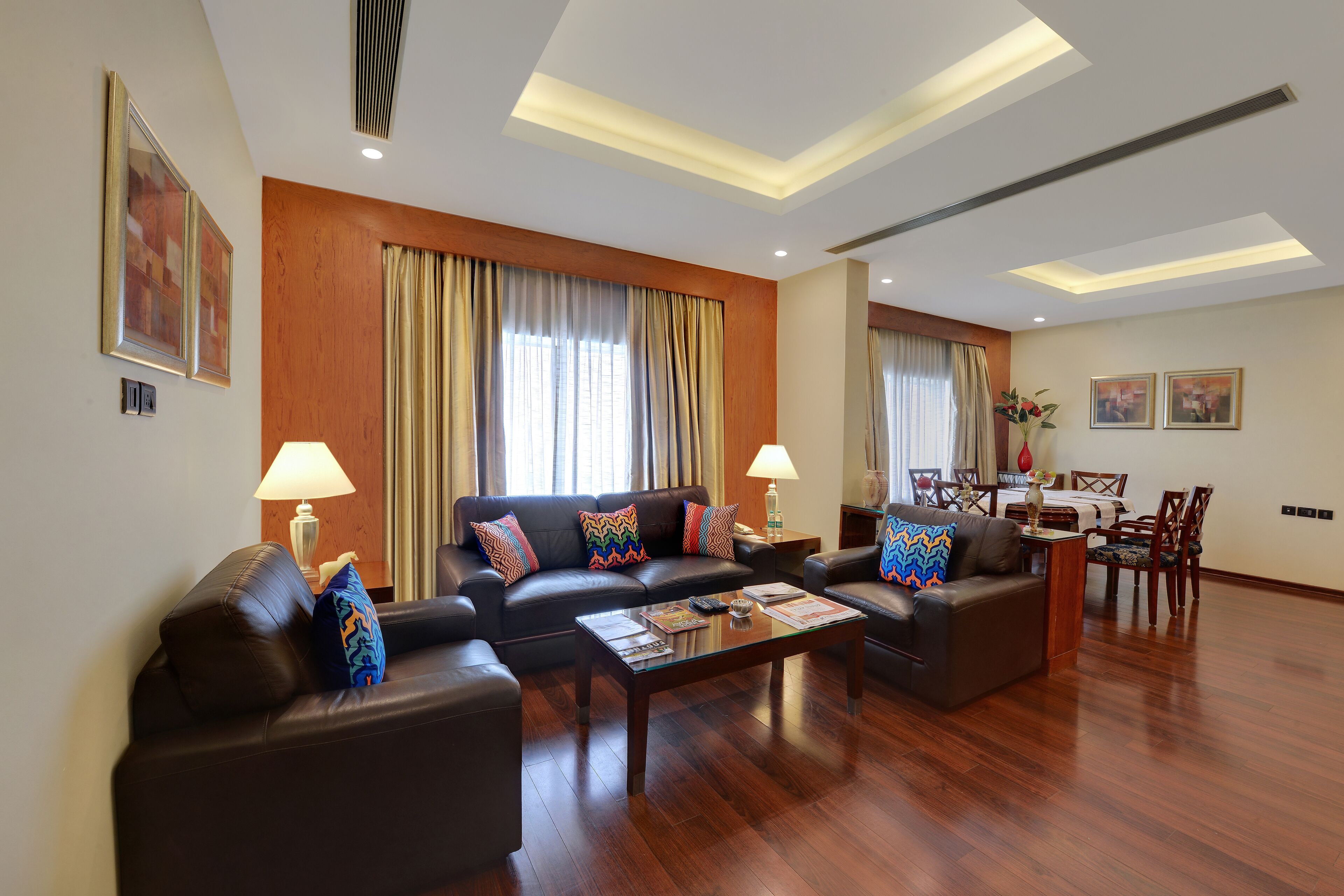 A spacious living room with a modern design, featuring a large sofa set, a coffee table, and a dining area with a table and chairs.