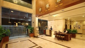 Un vestíbulo de hotel con una recepción, una zona de espera con sillas y un gran ventanal que da a la entrada.