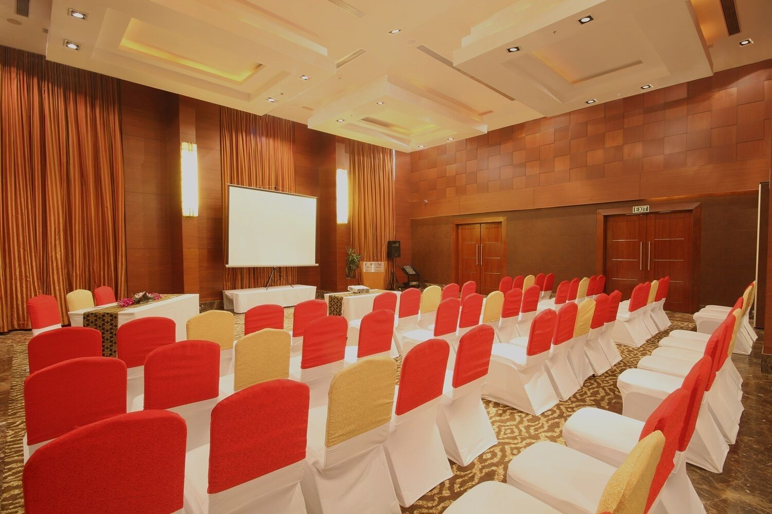 A conference room with rows of chairs, a projection screen, and an exit door.