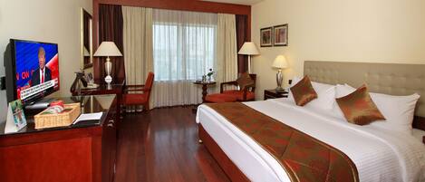 A hotel room with a large bed, a desk with a television, a chair, and a lamp.