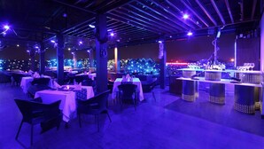 Un restaurante al aire libre con mesas, sillas, zona de bar e iluminación decorativa.