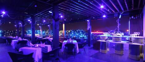 An outdoor restaurant with tables and chairs, a bar area, and decorative lighting.