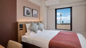 A hotel room with a bed, a window with a cityscape view, and a wall-mounted air conditioning unit.