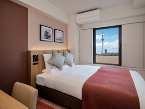 A hotel room with a bed, a window with a cityscape view, and a wall-mounted air conditioning unit. - Hotel MyStays Asakusa (Tokyo)