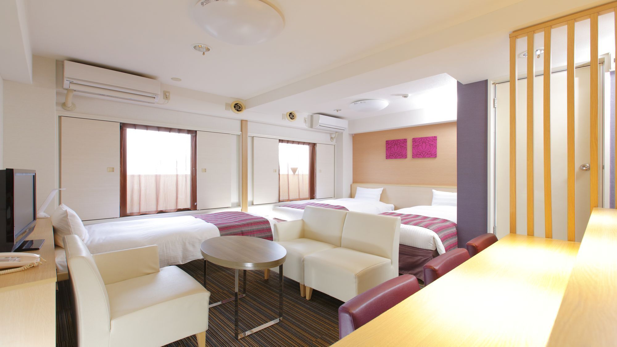 A hotel room with two beds, a desk, a chair, a small table, and a TV.