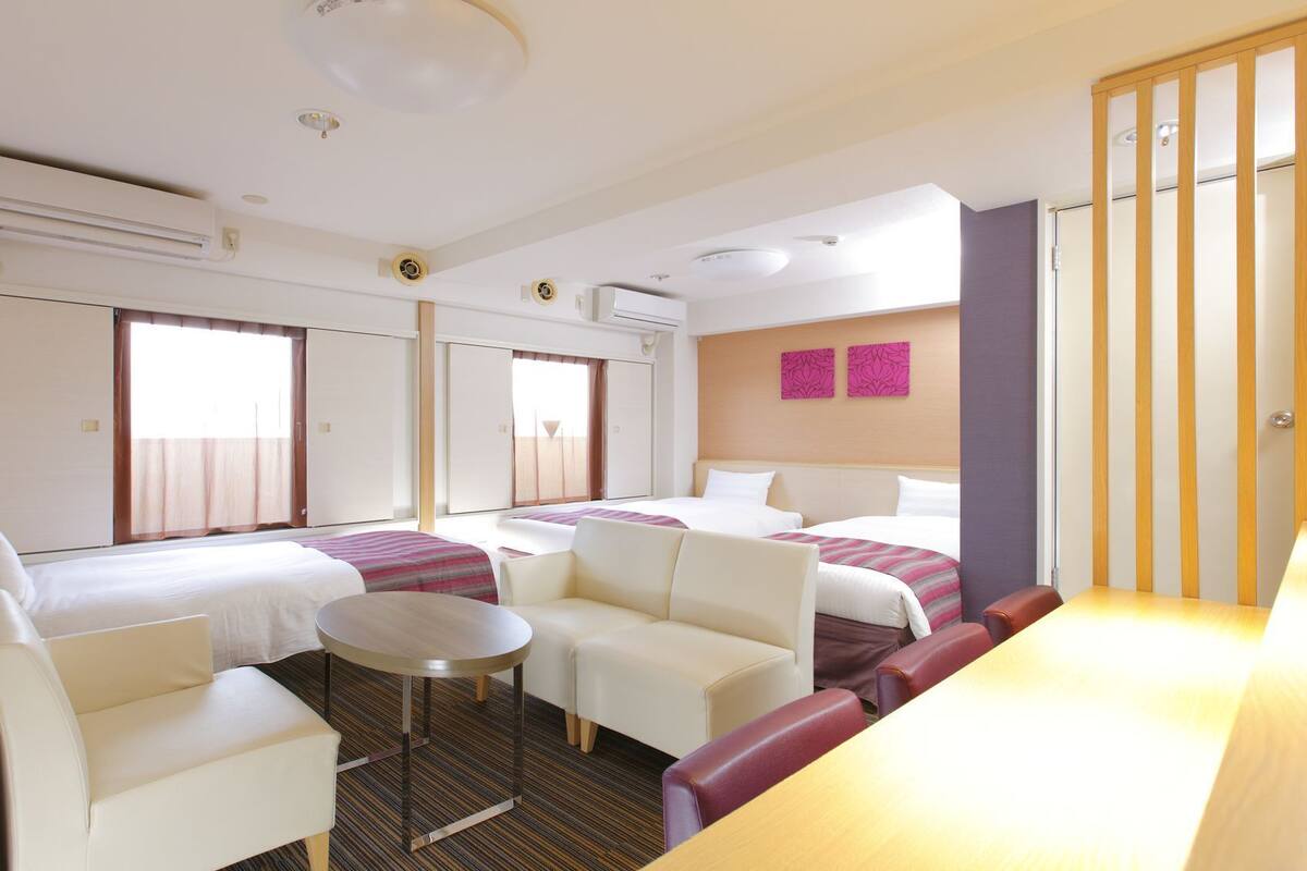 A hotel room with two beds, a desk, a chair, a small table, and a TV.