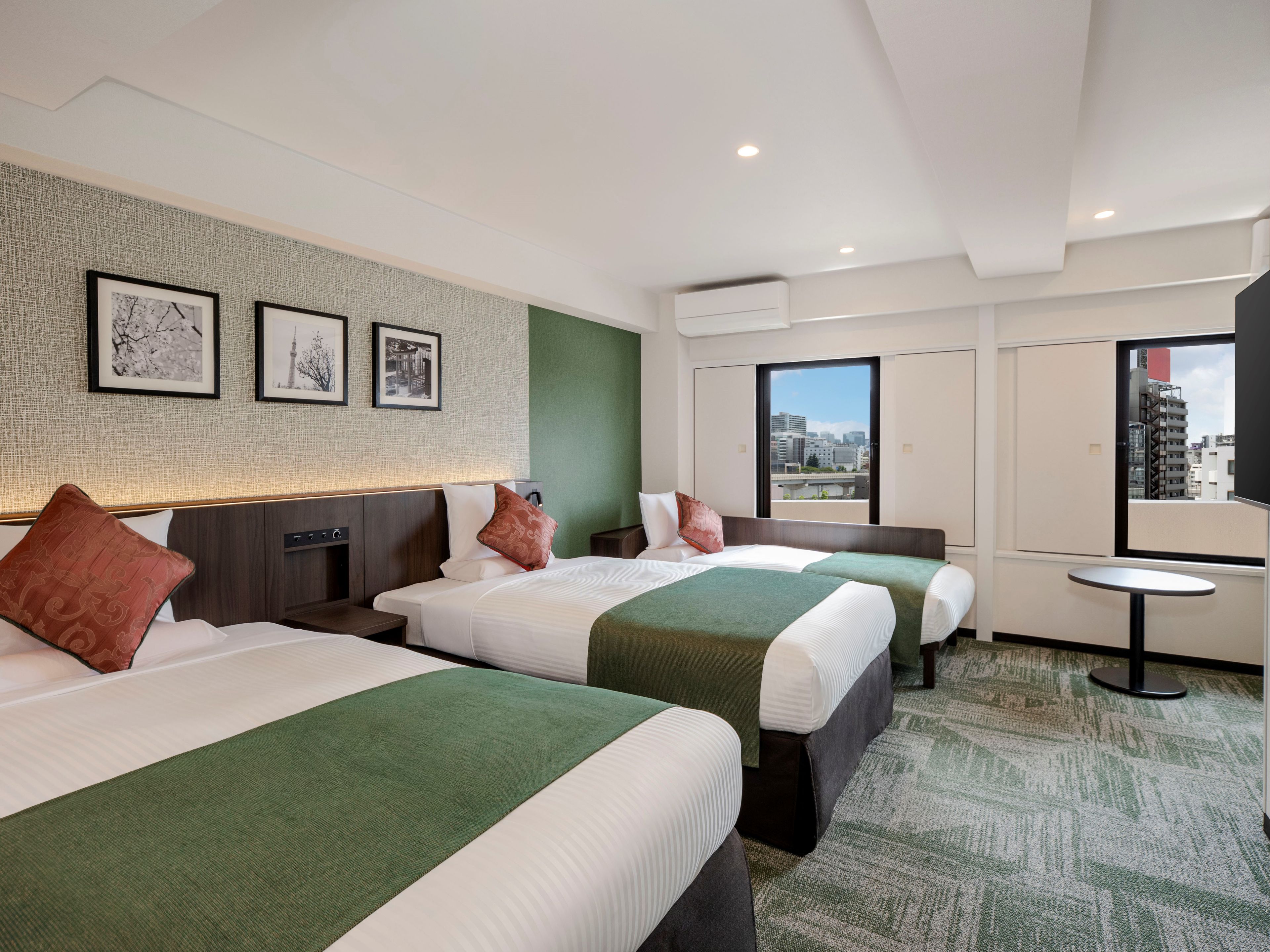 A hotel room with three beds, a green carpet, and a city view.